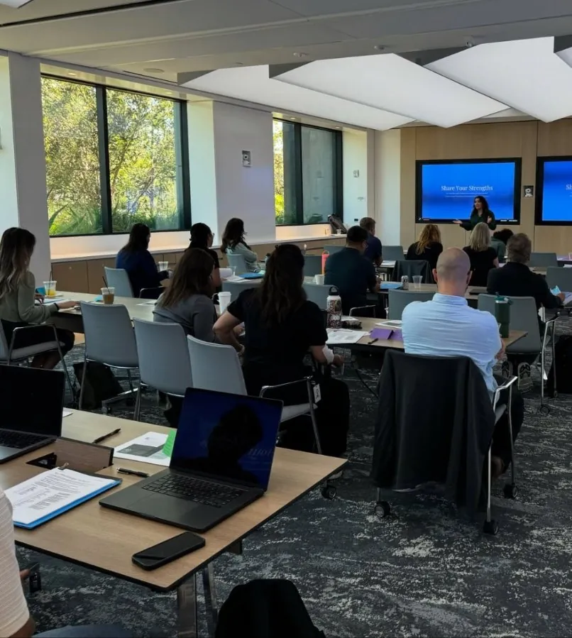 Workshop attendees seated at tables facing a screen that reads Share Your Strengths